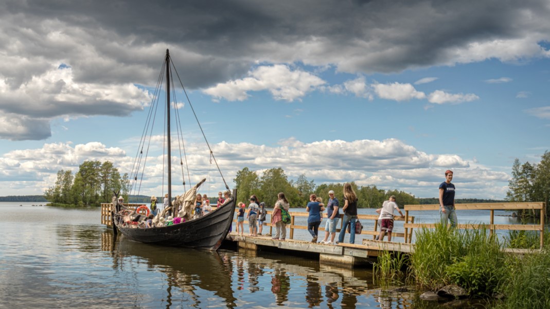 Vanha viikinkivene, laiturilta ottamassa ihmisiä kyytiin.